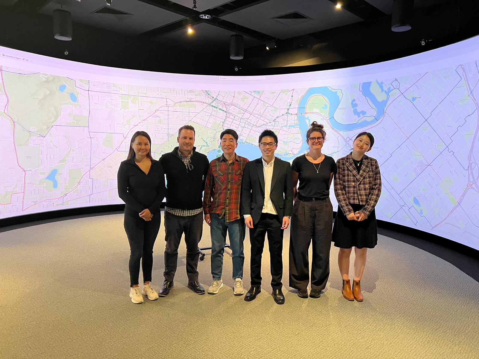 Group of people standing in front of a massive curved screen with a map of Perth on it.